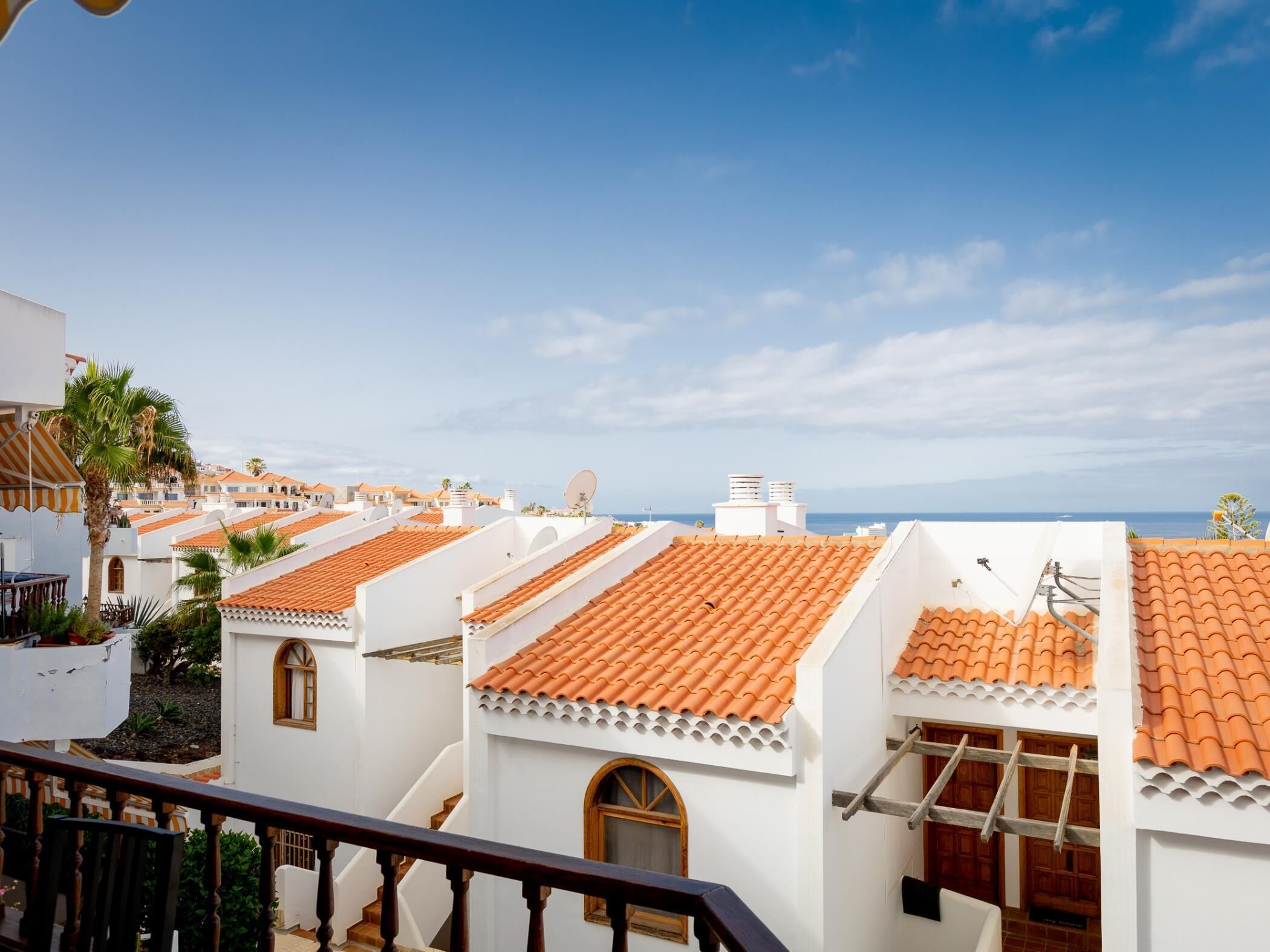 A coastal residential area with terracotta-tiled roofs, white walls, and a clear view of the sea.