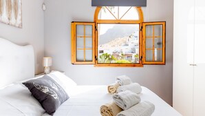 A bedroom with a bed, a window with open shutters, and a view of a hillside. - 21 C Apartamento Las Bouganvillas (Costa Adeje)