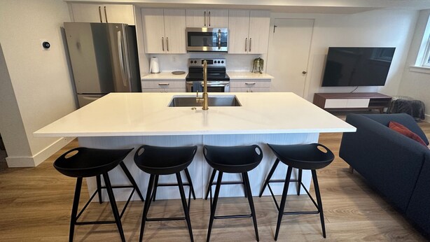 Una cocina moderna con una isla central, taburetes de bar, horno empotrado y un televisor grande.
