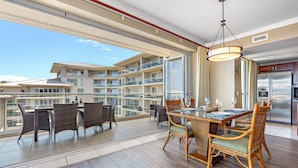 A balcony with wicker furniture, a dining table with chairs, a large window, and a modern kitchen with a refrigerator.