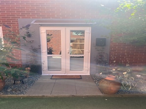 Enter a charming home through the white-framed glass door, surrounded by a brick wall and lush artificial grass.