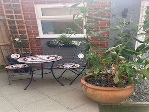 Relax in this charming outdoor seating area with a metal table and chairs, surrounded by a lush plant and a brick wall.