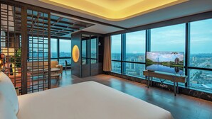 Quarto de hotel moderno com uma cama grande, área de estar com vista e uma televisão em suporte.