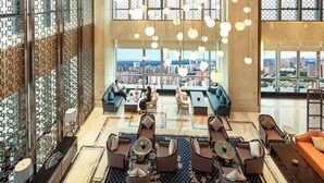 Um hall amplo com vista para a cidade, assentos modernos e luminárias esféricas penduradas.
