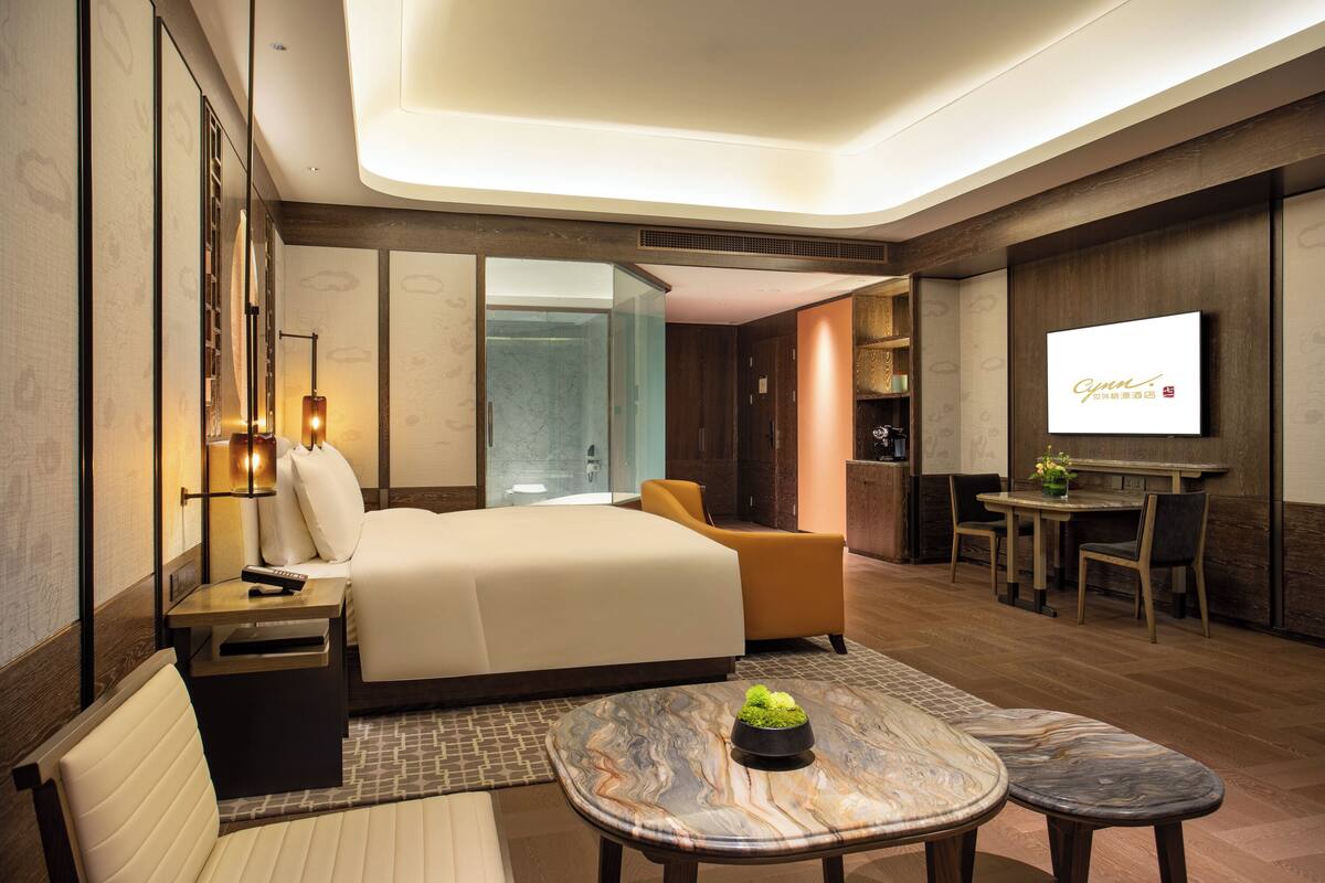 A hotel room with a bed, a sofa, a dining table, and a TV.
