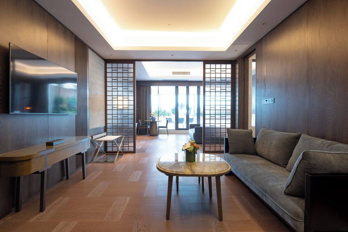 A modern living room with a sofa, a coffee table, a TV, and a view through a glass door.
