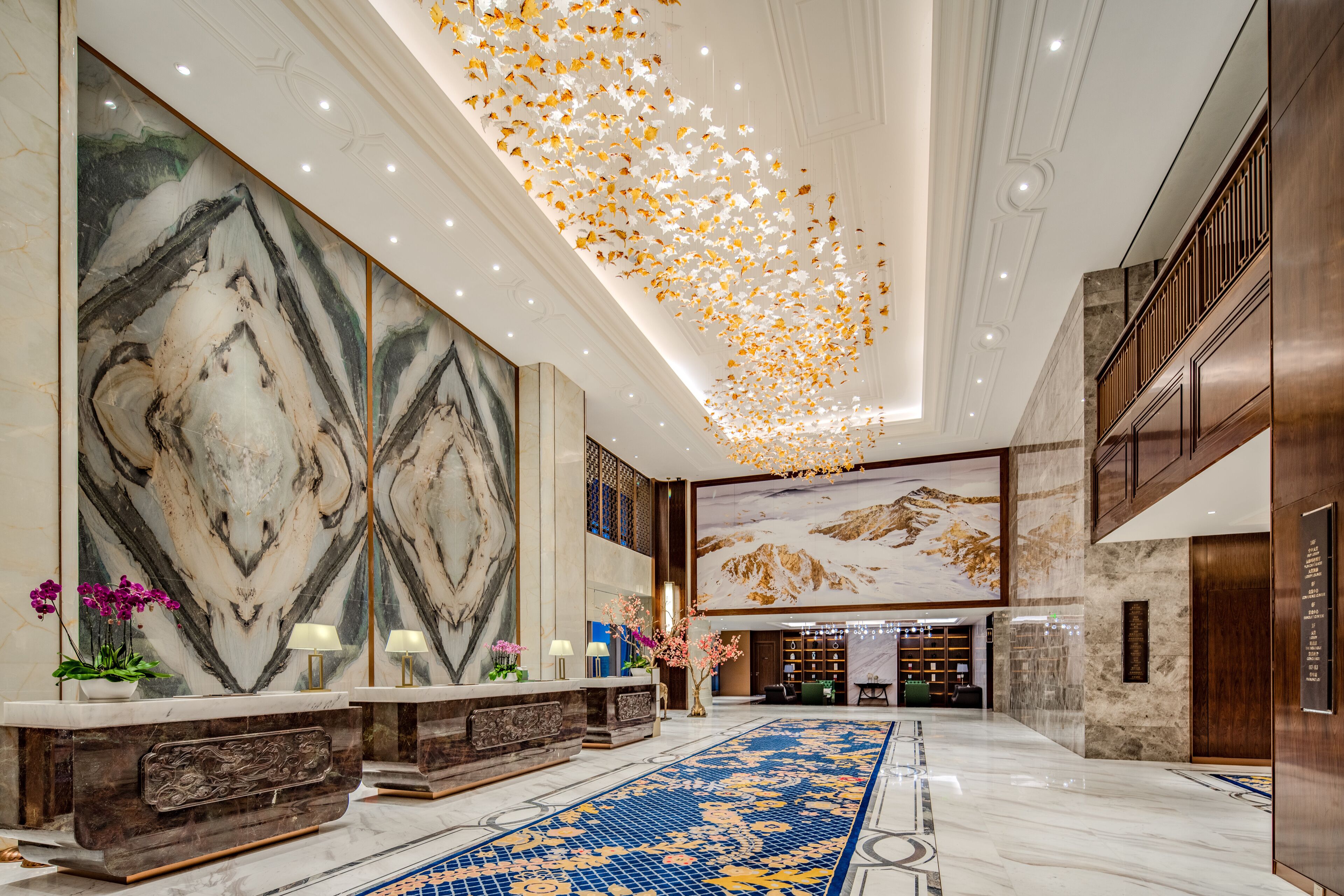 Un hall d’entrée spacieux avec un comptoir de réception en marbre, une grande fresque murale et une moquette à motifs.