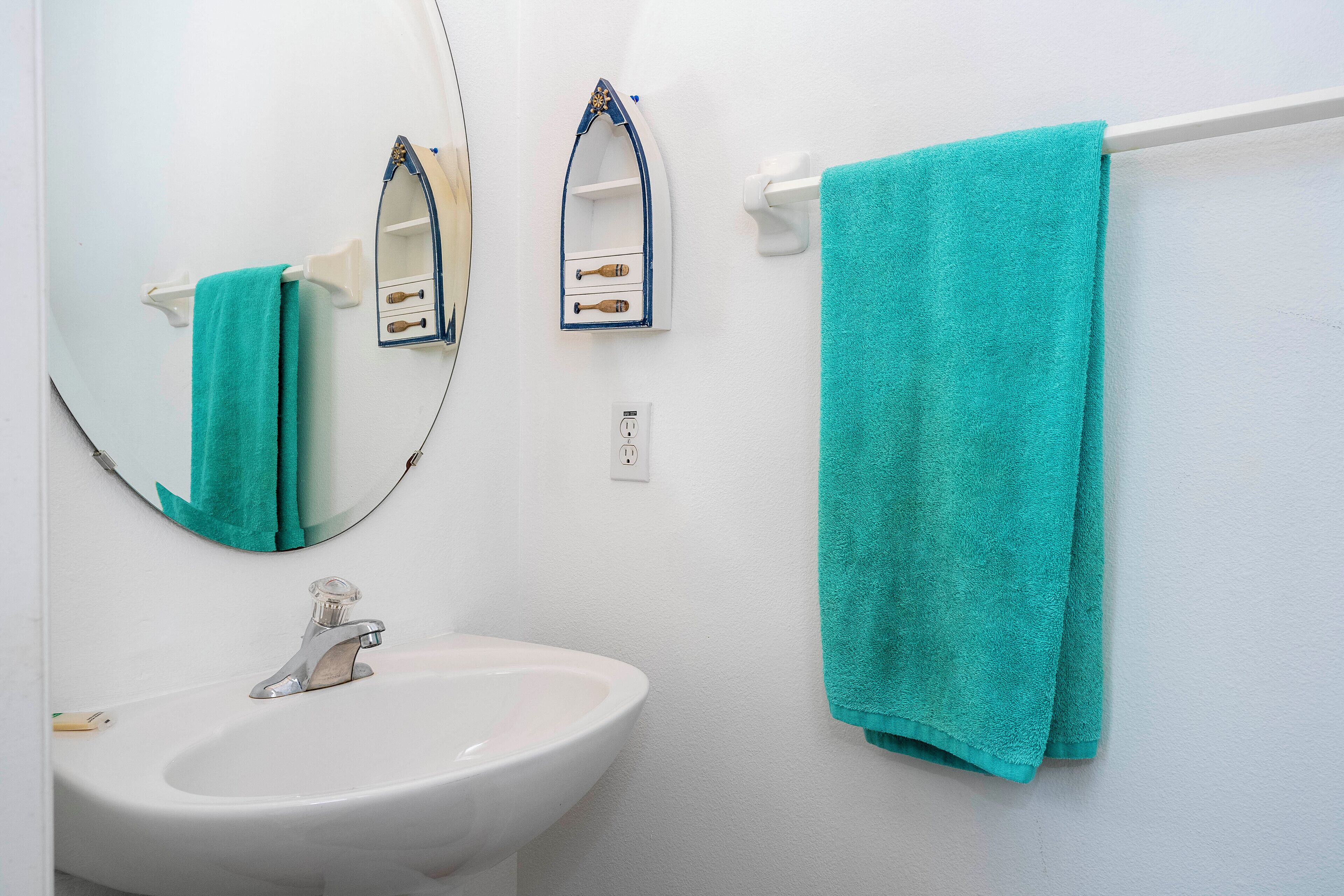 Une salle de bain avec un lavabo blanc, un miroir et une serviette turquoise suspendue à un porte-serviettes.