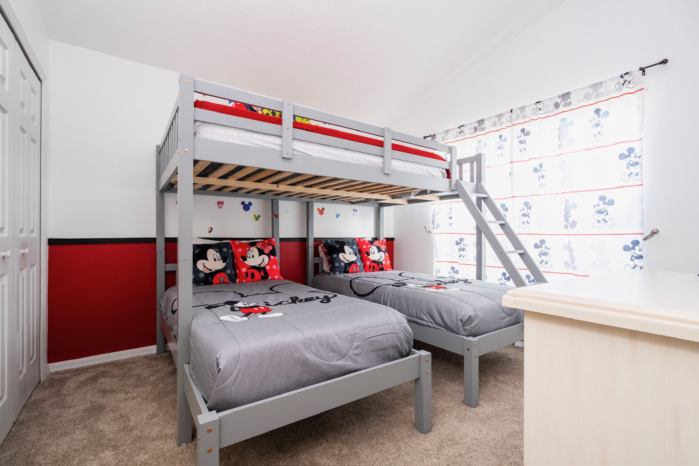 Une chambre avec un lit superposé, de la literie aux motifs de Mickey Mouse, un bureau et une fenêtre avec un rideau à l’effigie de Mickey Mouse.