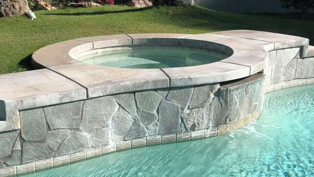 Ein Schwimmbecken mit Steinrand und ein Whirlpool.