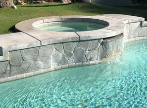 A swimming pool with a stone border and a hot tub.
