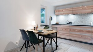A modern kitchen with wooden cabinets, a dining table with chairs, and a window with a view of greenery. - Apartment "City Ravensburg" with Balcony and Wi-Fi (Ravensburg)