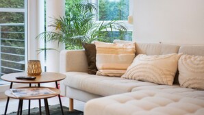 A modern living room with a sofa, a small round table, a potted plant, and a view of greenery outside. - Apartment "City Ravensburg" with Balcony and Wi-Fi (Ravensburg)