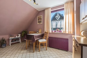 A dining area with a table, chairs, a radiator, a window with curtains, and a plant. - Apartment 'Am Ps Speicher' with Balcony and Wi-Fi (Einbeck / Wenzen)