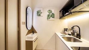 Una cocina moderna con encimera blanca, pileta de acero inoxidable y grifo negro. Hay dos espejos empotrados en la pared e impresiones botánicas enmarcadas.