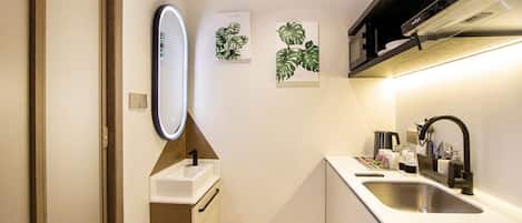 Una cocina moderna con encimera blanca, pileta de acero inoxidable y grifo negro. Hay dos espejos empotrados en la pared e impresiones botánicas enmarcadas.