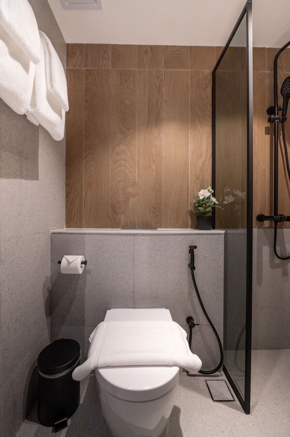 Une salle de bain moderne avec des toilettes, une poubelle noire, un espace douche et une petite plante en pot.