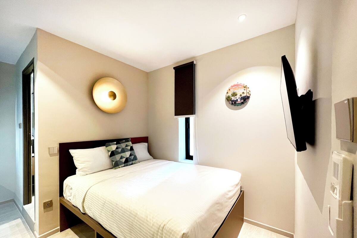 Una camera da letto moderna con un letto, una TV a parete e un originale lampadario a forma circolare.