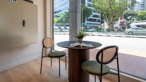Un interior moderno con una mesa redonda, dos sillas, una planta en maceta y vistas a una calle de la ciudad a través de ventanas amplias.