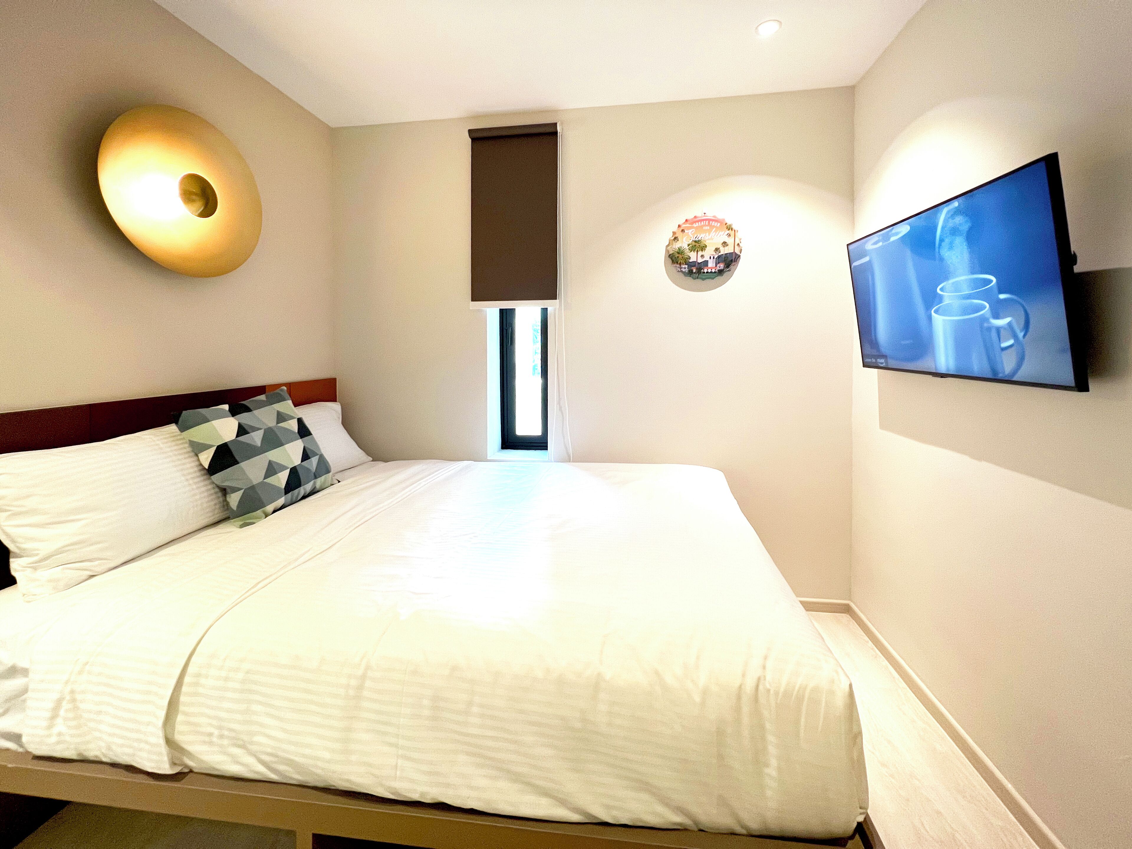Habitación de hotel con cama, televisor de pared y ventana con vistas a palmeras.