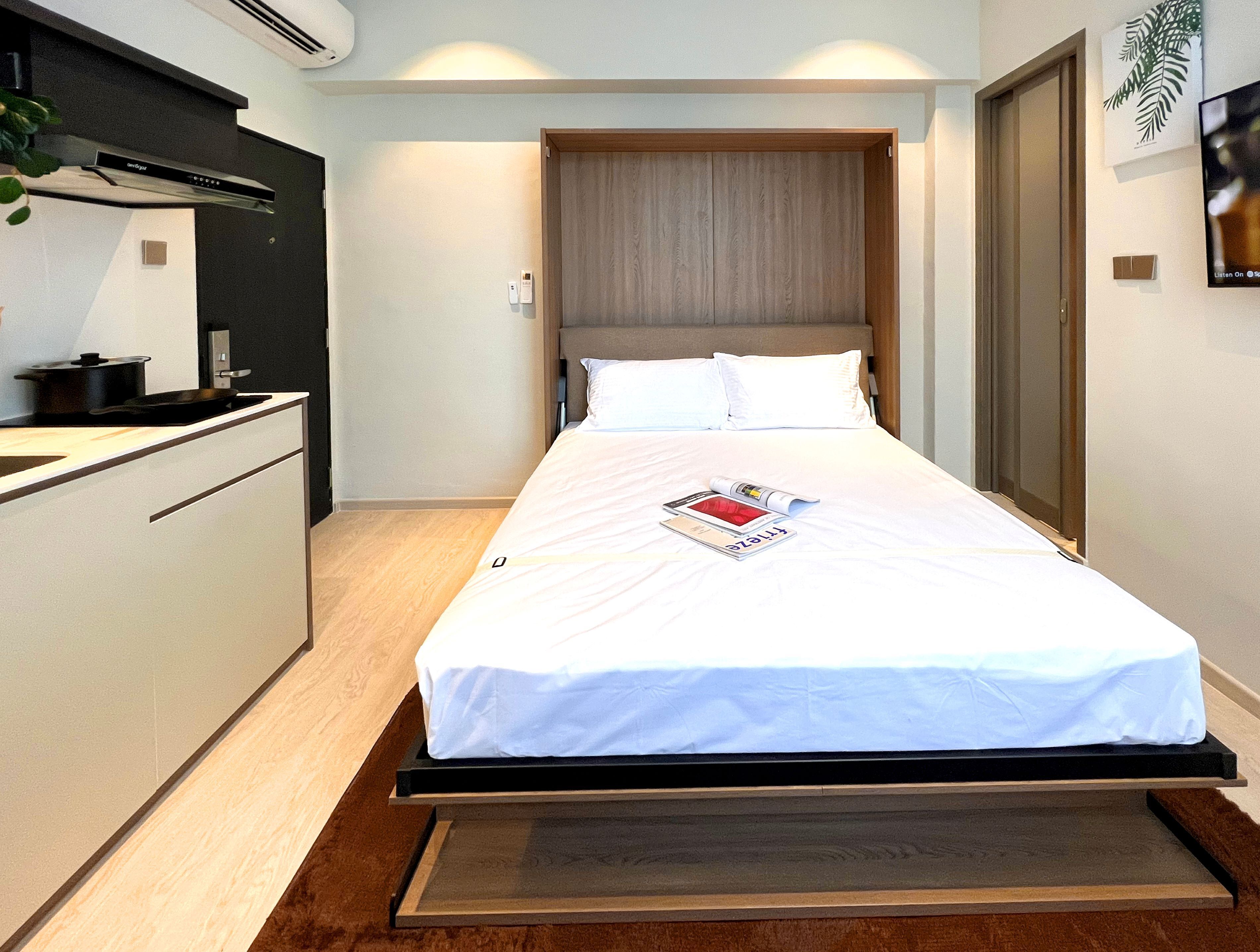 Une chambre d’hôtel compacte comprenant un lit, une petite kitchenette et un plancher en bois.