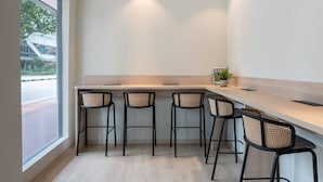 Zona de bar moderna con cuatro taburetes negros, una encimera de color claro y una planta en maceta.