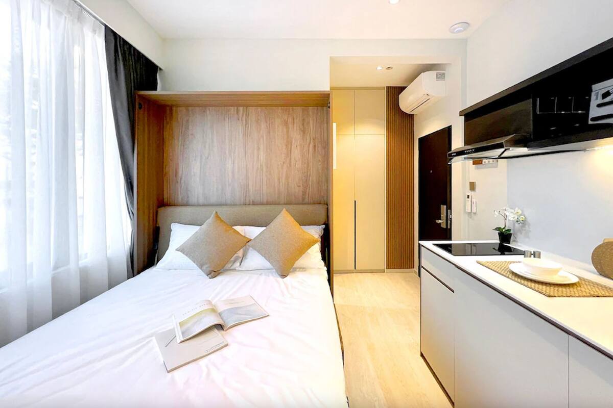 A modern hotel room with a large bed, a small kitchenette, and a view of the city.