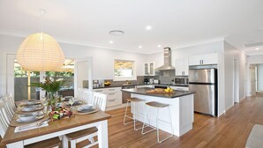 Een moderne keuken met een centraal eiland, roestvrijstalen apparatuur, en een eethoek met een houten tafel en witte stoelen.