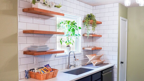 Een keuken met witte metro betegeling, houten planken, een raam met een plant en een vaatwasser.