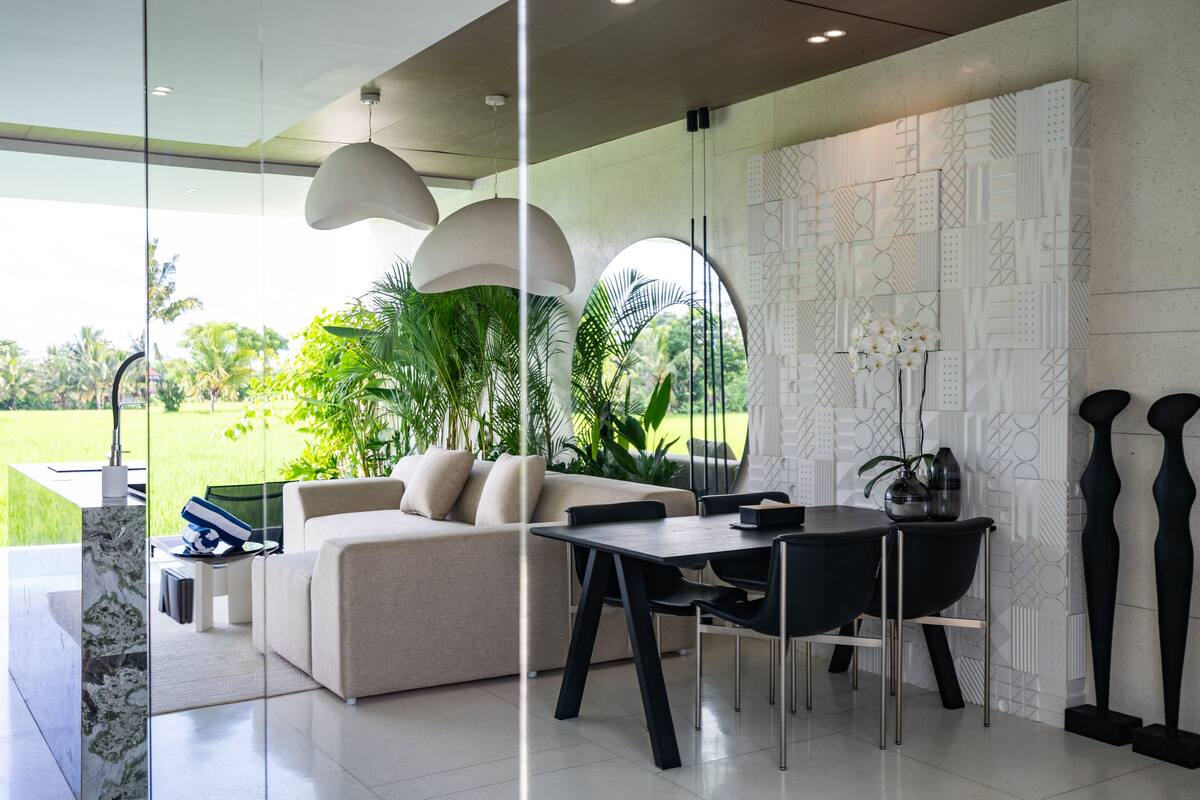 Una sala moderna con sofá, mesa de comedor y sillas, un ventanal con vistas a zonas verdes, y decoración mural.