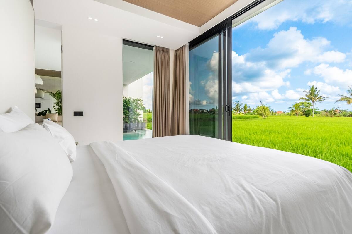 Un dormitorio moderno con una cama grande, un panel de vidrio corredera que da a una piscina y vistas a un campo verde.