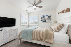 Un dormitorio con cama, ventilador de techo, televisor y ventana con persianas.