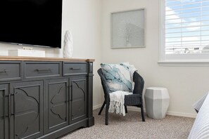 A bedroom with a dark wooden dresser, a television, a chair with a patterned cushion, a white speaker, and a framed picture on the wall. - The Salty Escape at Dunes w/ firepit & beach toys (Oceano)