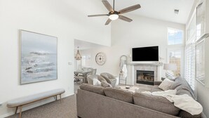 A living room with a sofa, a fireplace, a television, and a ceiling fan.