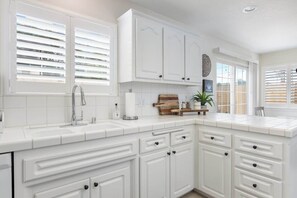 Cocina con armarios blancos, un lavamanos y una ventana con persianas.