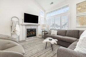 A living room with a fireplace, a flat-screen TV, a sofa, and a coffee table. - The Salty Escape at Dunes w/ firepit & beach toys (Oceano)