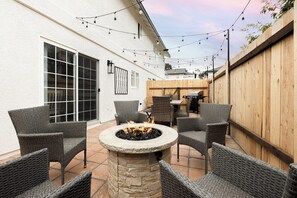 Un patio al aire libre con mobiliario de mimbre, un hogar de piedra y luces colgantes.