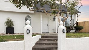 A white house with a front door, a set of concrete steps leading up to the entrance, and a tree with a curved branch overhanging the steps.