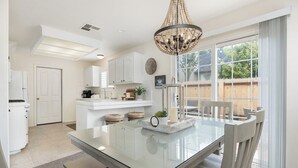 A modern kitchen with white cabinets, a glass dining table, and a chandelier.
