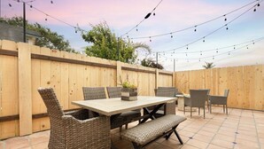 An outdoor patio with a wooden table and wicker chairs, surrounded by a wooden fence.