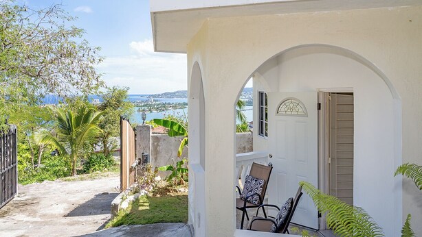 A white building with a covered porch, a door, and a chair with a patterned cushion.