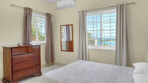 A bedroom with a bed, a dresser, a window with curtains, and an air conditioning unit.