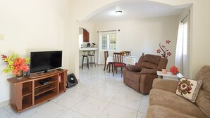 A living room with a TV, sofa, and a dining area with chairs and a table.