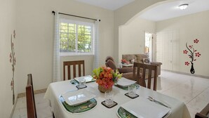 A dining area with a table set for four, a window with curtains, and a sofa in the background.
