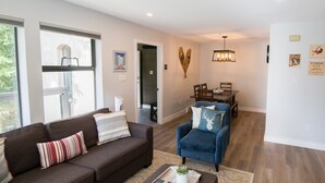 A modern living room with a brown sofa, blue armchair, and a dining area with a wooden table and chairs. - Modern and bright Snowberry condo on Blackcomb Mountain (Whistler)