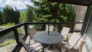 A balcony with a round table and four chairs, overlooking a forested area with mountains in the distance. - Modern and bright Snowberry condo on Blackcomb Mountain (Whistler)
