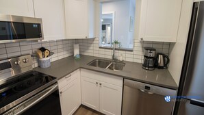 A modern kitchen with white cabinets, stainless steel appliances, a double sink, and a coffee maker. - Modern and bright Snowberry condo on Blackcomb Mountain (Whistler)