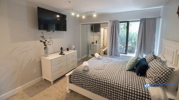 A bedroom with a bed, a dresser, a TV mounted on the wall, and a window with curtains. - Modern and bright Snowberry condo on Blackcomb Mountain (Whistler)