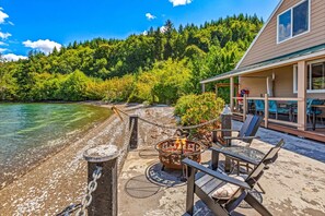 A lakeside patio with outdoor seating, a fire pit, and a view of a forested area. - Utopia Cove in Union (Union)