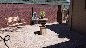 Ein Patio mit Backsteinmauer, einer Bank, einem Ziergartenbeet und einem Metalltor.